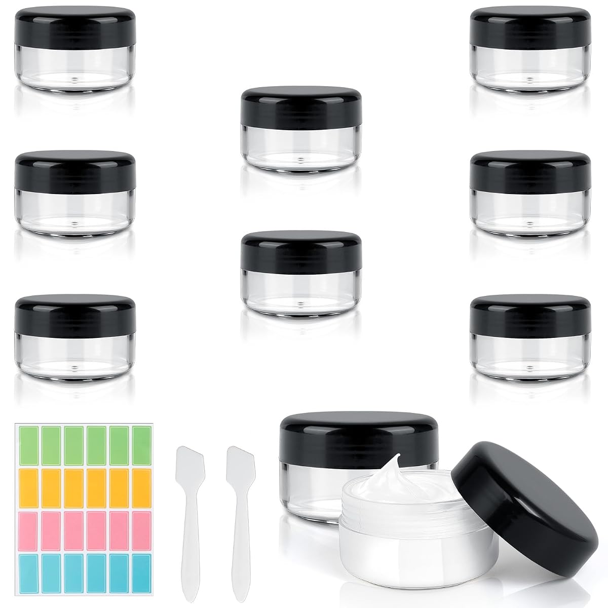Huit pots cosmétiques transparents avec deux spatules et 24 étiquettes, prêts à rejoindre une trousse de voyage.