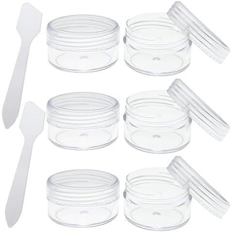 Six pots de voyage transparents de 10 ml et deux mini spatules posés près d’une trousse.