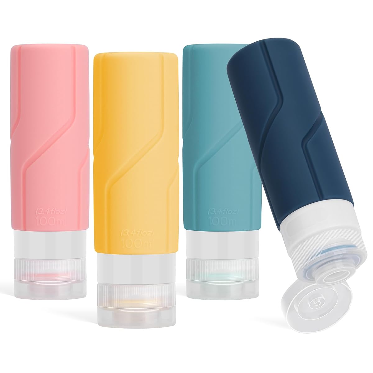 Quatre flacons souples de voyage en silicone, aux coloris variés, posés près d’une trousse de toilette.